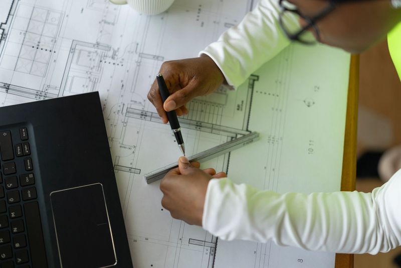 Architect working on architectural blueprint, utilizing pen and ruler to create a detailed construction layout in a modern office setting