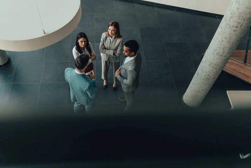 Diverse team of professionals gathers in a sleek, contemporary lobby, engaged in discussion. The scene conveys collaboration, networking, and business culture in a stylish office environment.