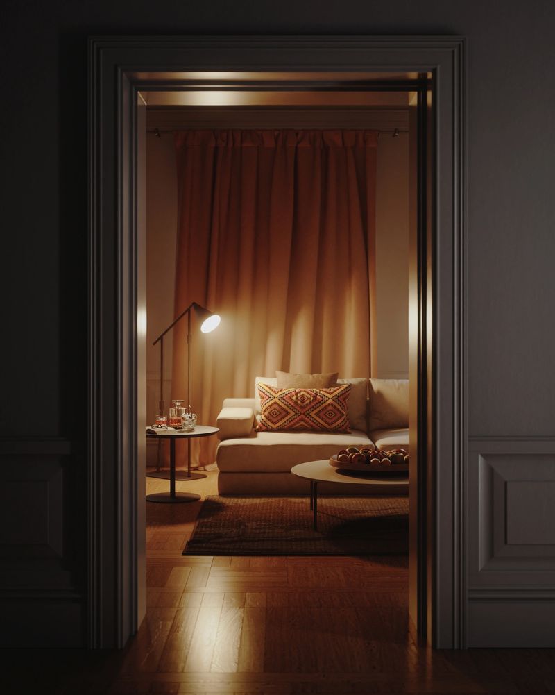 Digitally generated moody interior scene showing a cozy modern living room framed by an open doorway at night. A soft beige sofa with a patterned accent pillow, floor lamp, side table with glass decanter and drinks, and a low coffee table with fruit bowl sit in front of warm brown curtains, all reflected subtly in the polished wooden floor. Atmospheric low-key lighting, rich earth tones, and empty space create a cinematic, intimate mood perfect for concepts of comfort, hygge, home décor, and relaxed evening lifestyle.