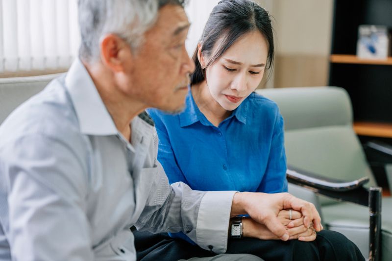 Asian adult offspring daughter holding hands with Asian senior man in emotional support moment at clinic, Bangkok