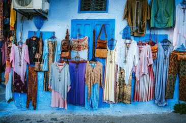 Colorful traditional clothes and bags displayed on a bright blue wall.