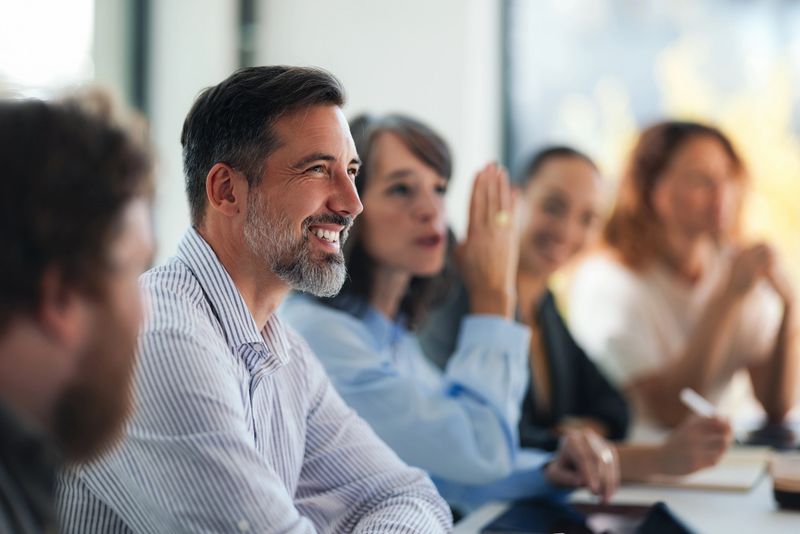 A group of professionals gathering in a sunny, modern office, sharing ideas, smiling and engaging in a collaborative meeting. Perfect for business, teamwork, and workplace communication themes.