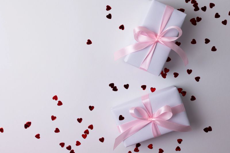 White Gift Boxes With Golden Ribbons, Top View On Beige Background Scattered With Gold Confetti And Curled