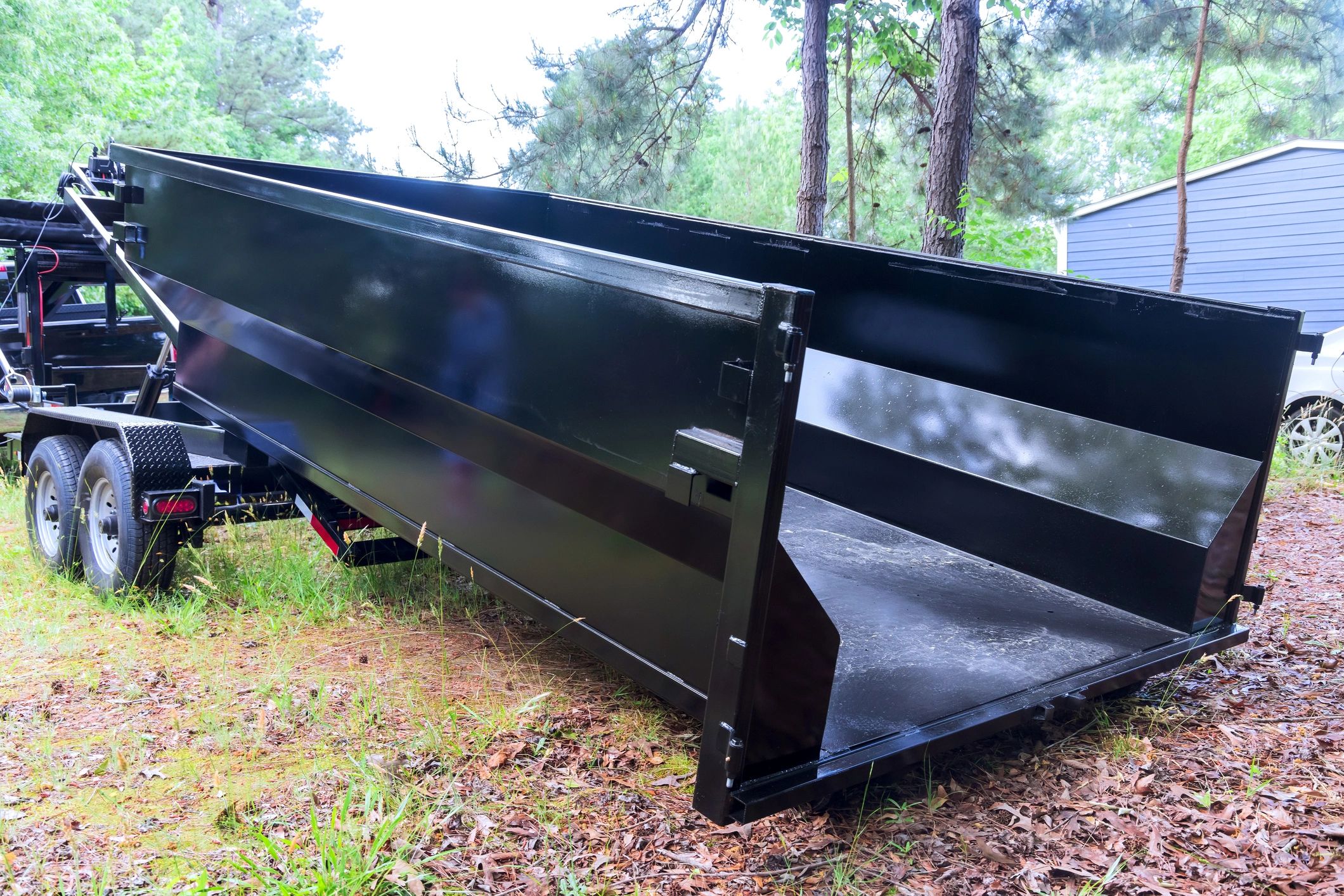 Black dump trailer with tall sides in a wooded area.