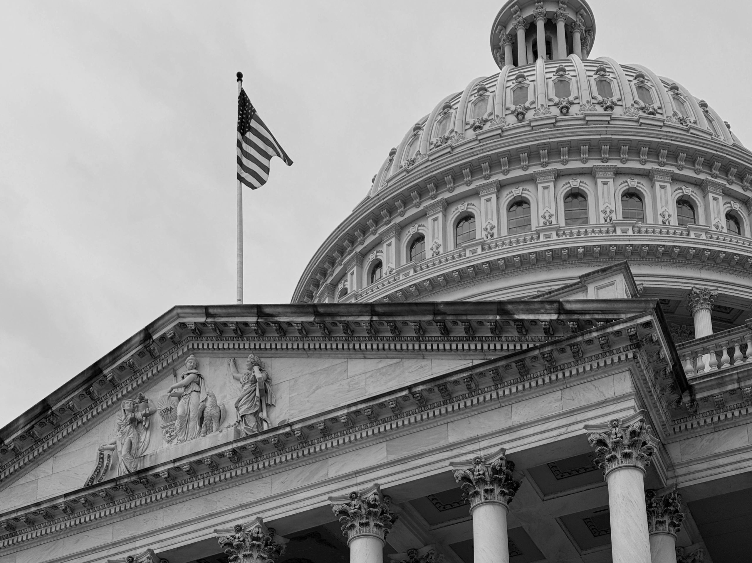 US Capitol dome and American flag on a cloudy day.