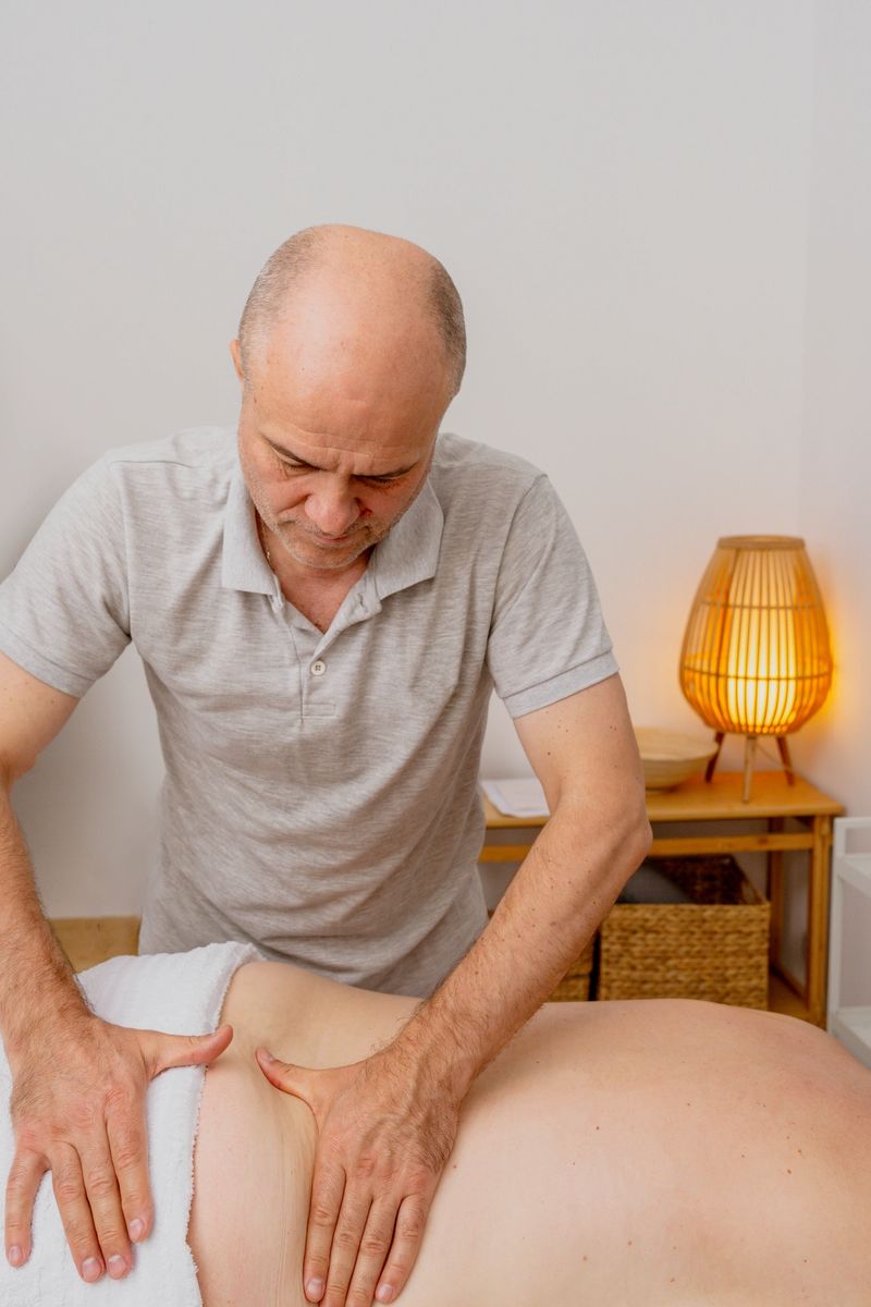 Male massage therapist applies pressure to a client's back in a calming treatment room, featuring warm lighting and natural decor elements