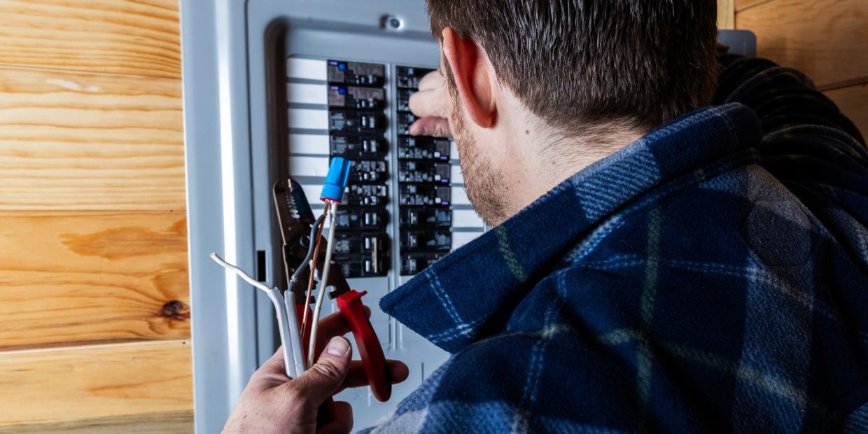 Man fixing an electrical panel with tools and wires.