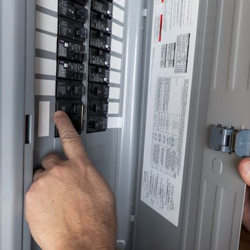 Person pointing at a circuit breaker in an electrical panel.