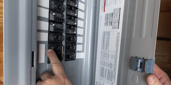 Hand operating a circuit breaker inside an electrical panel.