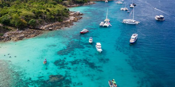 Boats anchored in clear blue waters near a lush green island.