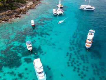 Boats anchored in clear blue water near a rocky shore.