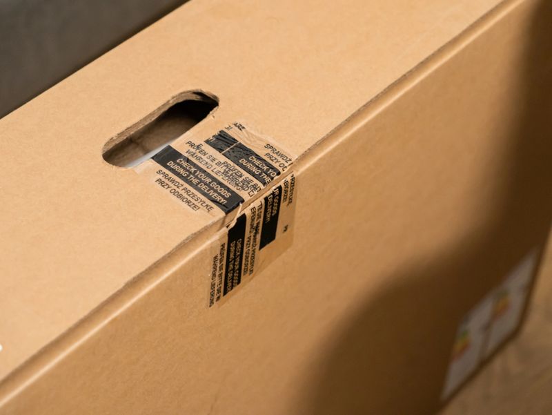 Close-up of a brown shipping carton, with robust carry handle and multilingual security tape, highlighting careful product inspection and secure delivery for online purchases