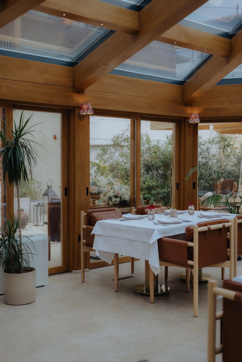 Sunny dining space with sophisticated table settings under a wooden framed glass ceiling, providing a bright, inviting atmosphere