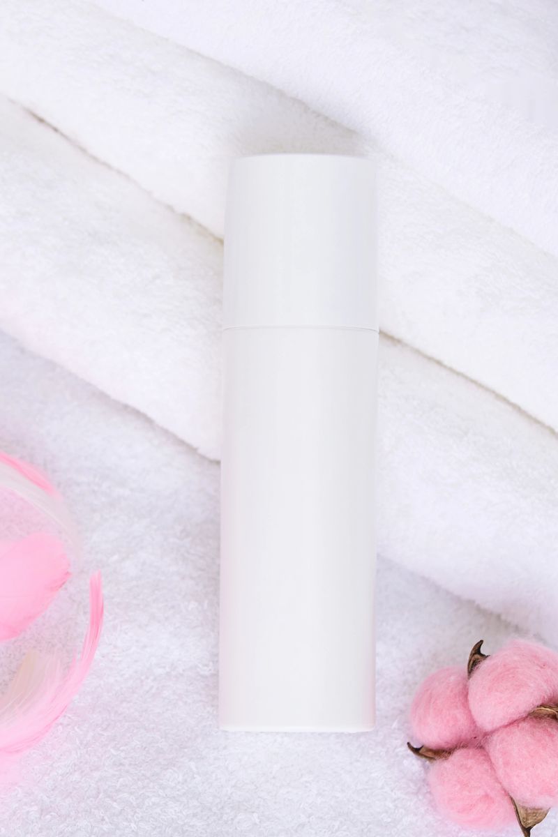 Minimalist skincare product on soft white towels with cotton and pink accents for a spa-like setting.