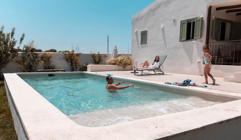 Family members relaxing and playing together by a private swimming pool on a warm, sunny day, representing a perfect summer holiday experience and quality time