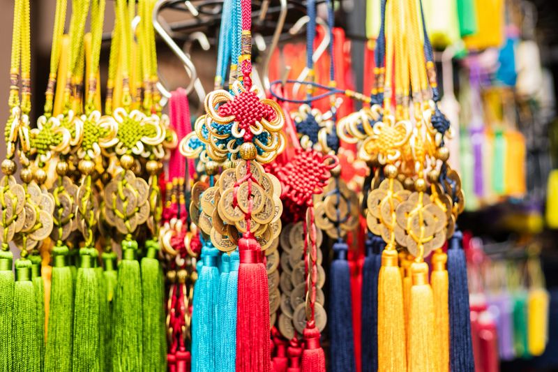 Tassels and charms are displayed on a rack at a market. They are made with different colors and materials. Shoppers can see the details in the sunlight during the day.