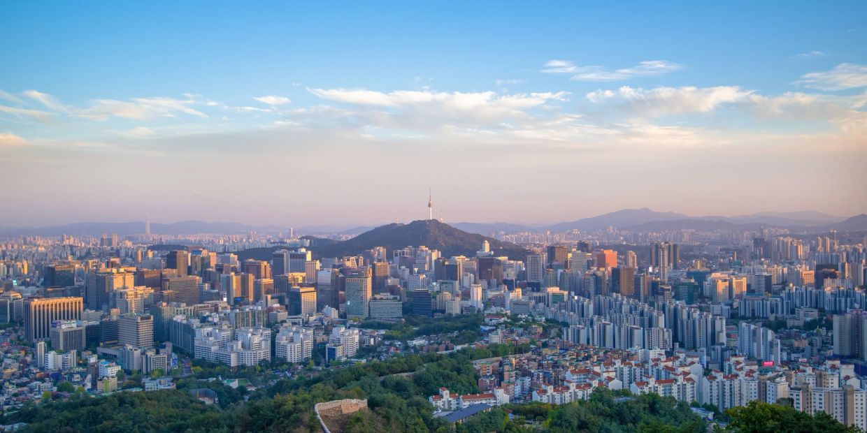 Panoramic cityscape with a central hill and tower under a blue sky.
