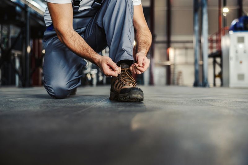Worker tying laces on sturdy safety boots on a factory floor, preparing for industrial tasks with focus on protection, durability and readiness for hands-on work