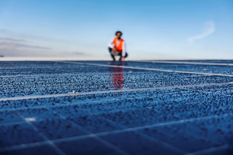 Engineer wearing a safety vest is checking solar panels covered in morning dew, ensuring optimal performance and maintenance of sustainable clean energy technology under a clear blue sky