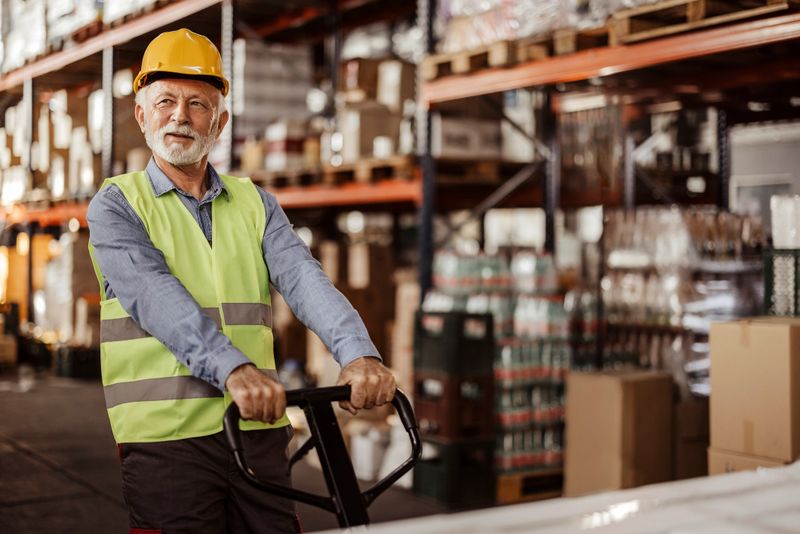 Senior warehouse worker dragging hand pallet truck or manual forklift with the shipment pallet unloading into a truck. Distribution, logistics import export operation, trading, shipment, delivery concept