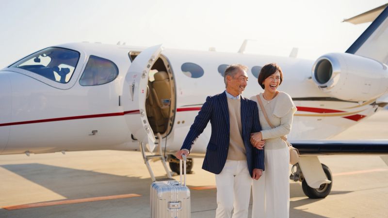 A senior couple is happily standing and posing for the camera next to a private jet before their flight.