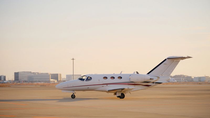 A stationary private jet at an airport runway during sunset.