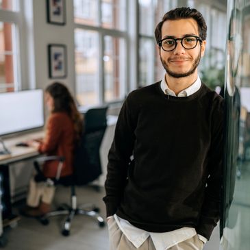 Young man with glasses smiling in a modern office environment.