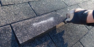 Hand wearing glove lifting a roof shingle.