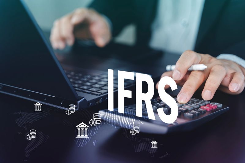 Business professional calculating figures with laptop and calculator with IFRS text overlay. Concept of international accounting standards, compliance, auditing, taxation, and global finance reporting.