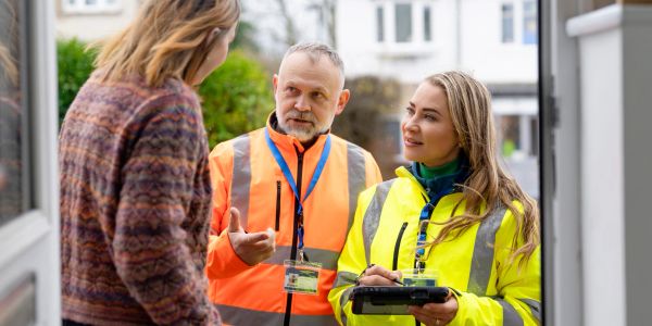 Two construction workers talking to a woman at her door.