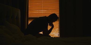 Silhouette of a person sitting on a bed in front of a window.