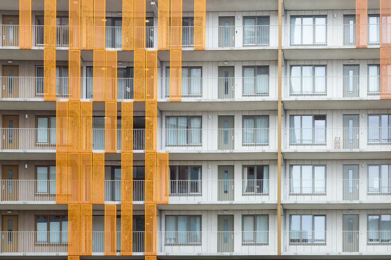 Contemporary residential building exterior with repeating balconies and orange architectural panels Zeeburgereiland in Amsterdam.