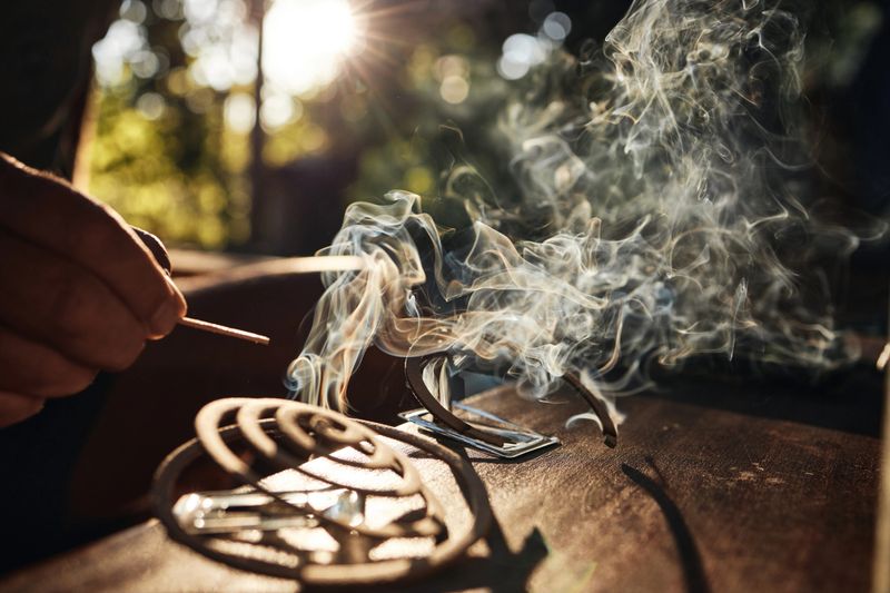 Person igniting a mosquito repellent coil with smoke rising in the bright outdoor sunlight