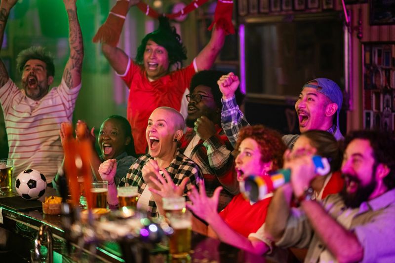 Diverse group of enthusiastic soccer fans cheering loudly watching a live game on tv at a bar or pub