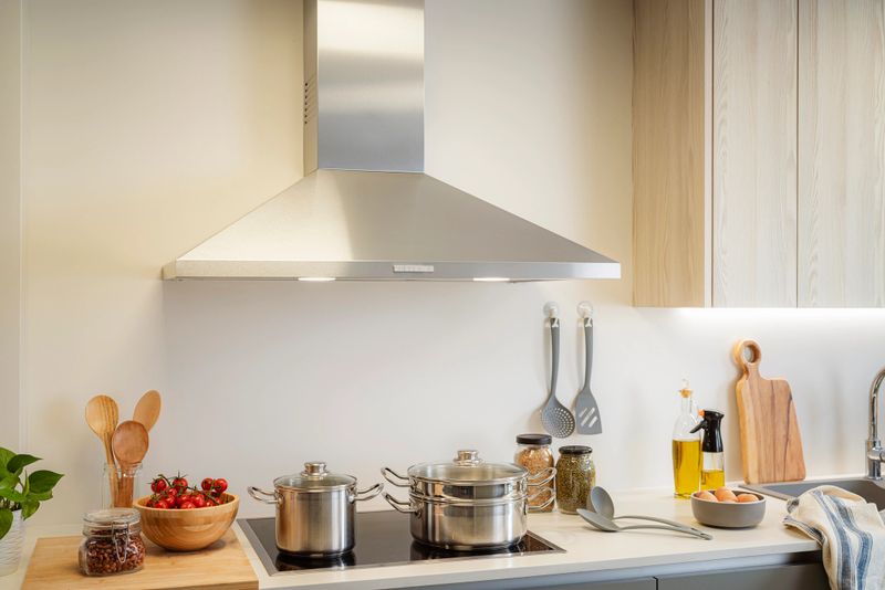 Stove and kitchen hood detail in a modern minimalist apartment. Cooking pots on stove, and wooden cutting board and utensils
