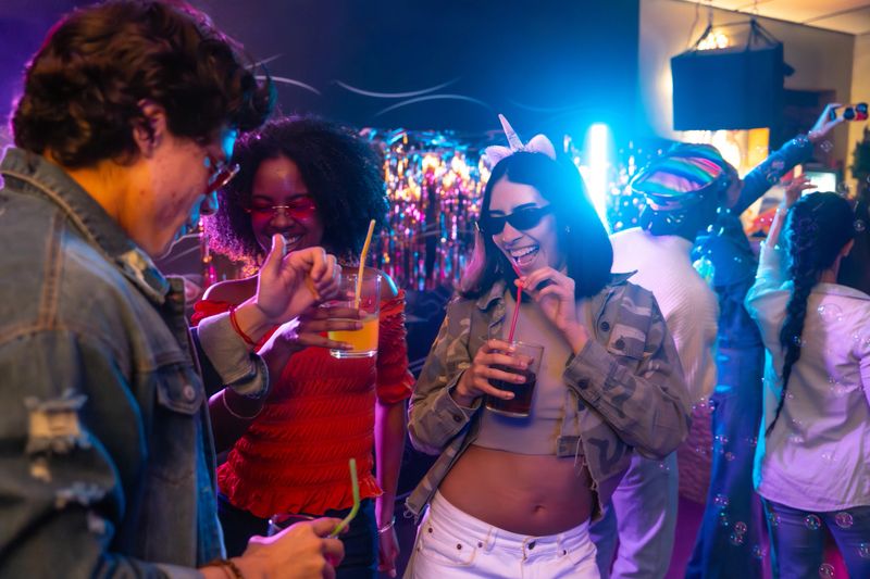 Diverse young adult friends laughing, drinking beverages, and enjoying the vibrant atmosphere at a night club or party, celebrating an event with music and colorful lights