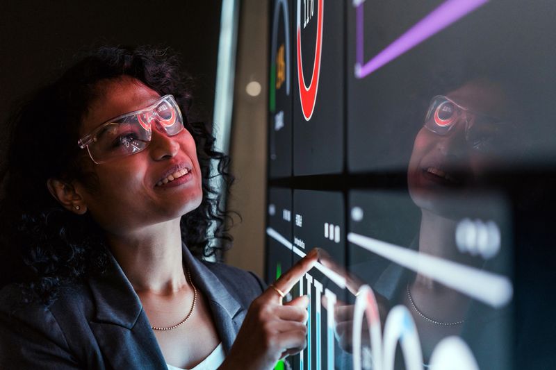 Analyst reviews colorful data dashboards on large digital screen in modern tech workspace. Scene reflects analytics, technology, research, metrics, insight, strategy, and data-driven analysis.