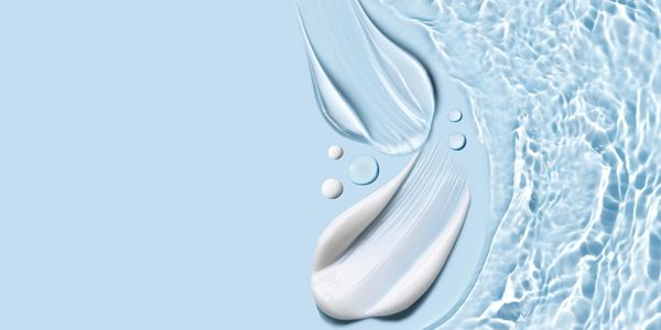 Close-up of creamy skincare product with water droplets on blue surface.