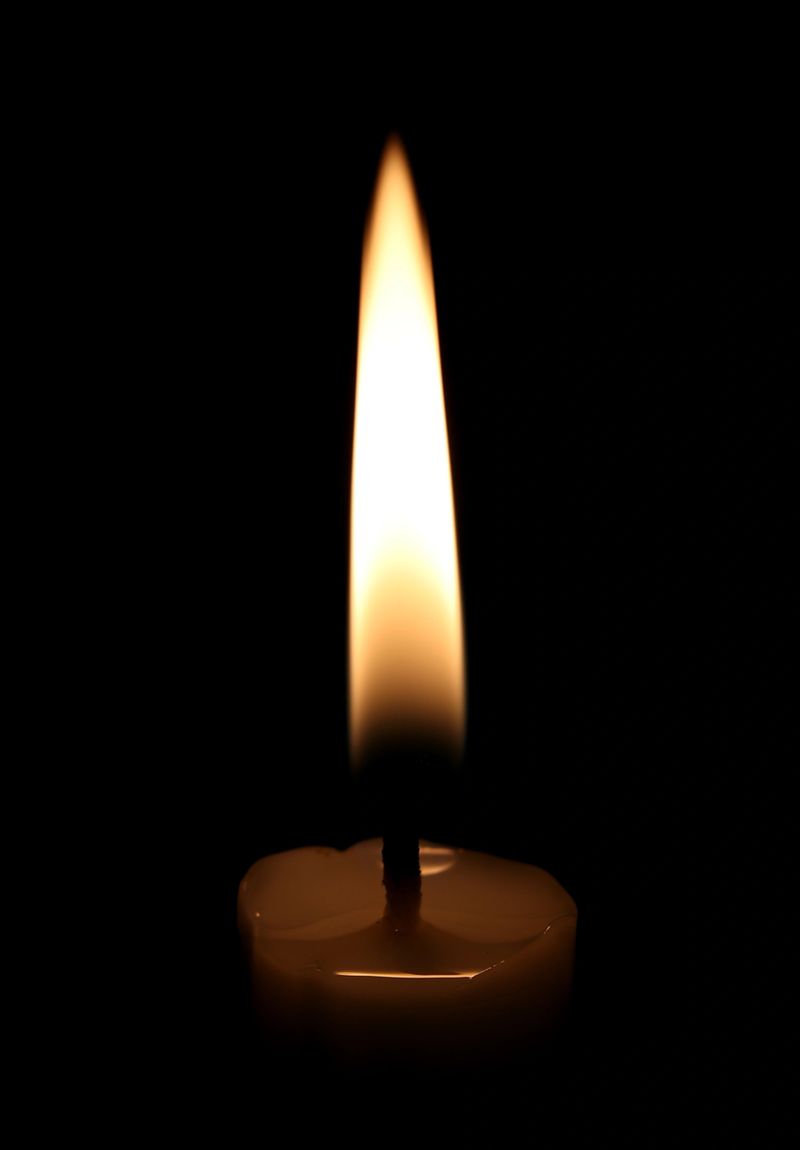 Single candle flame isolated on black background, centered vertical fire with warm glow creating calm and spiritual atmosphere. Minimal symbolic concept ideal for memorial, meditation, hope