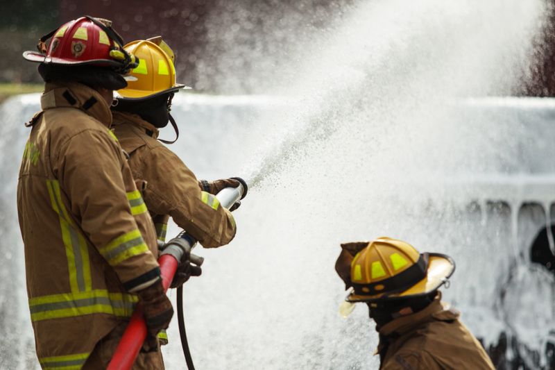 Firefighters working together spraying water foam to control flames during emergency firefighting operation. Concept of teamwork, fire suppression, emergency response, safety training, disaster prevention, and professional rescue service.