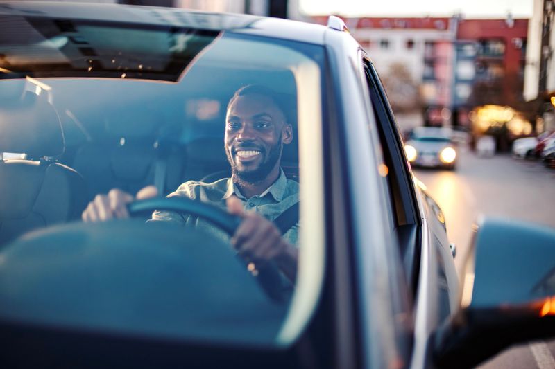 Smiling african american man driving a modern car on a city street during the day, enjoying his commute with a confident, content expression and hands on the steering wheel