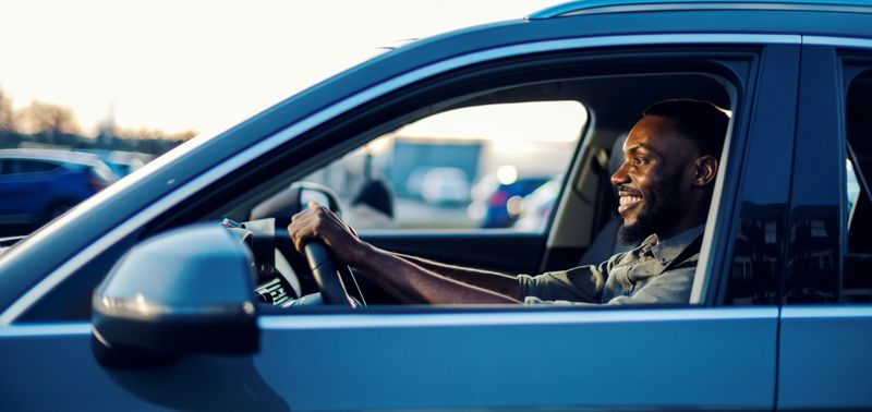 Young african-american man smiling while driving a modern car, enjoying a sunny commute or weekend road trip, confident, comfortable and relaxed behind the wheel