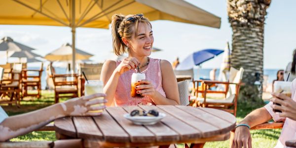 Young woman enjoying a drink outdoors with friends on a sunny day.
