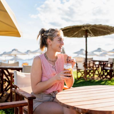 A woman enjoying a drink at an outdoor beachside café on a sunny day.