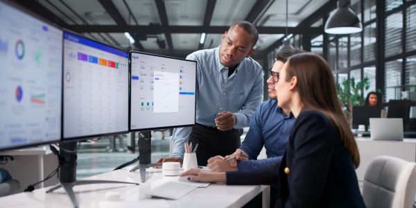 Team analyzing data on dual monitors in modern office.