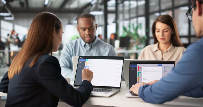 Diverse Team Discussing Support Tickets, Monitoring Downtime On Laptops. Professions: IT Technician, Consultant