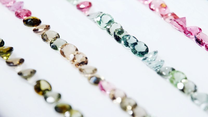 Rows of small colorful gemstones on white background.