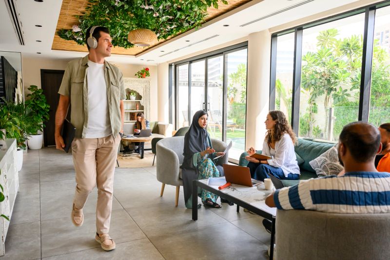 Diverse business professionals are collaborating and networking in a modern co-working space filled with natural light, plants, laptops, and contemporary furniture