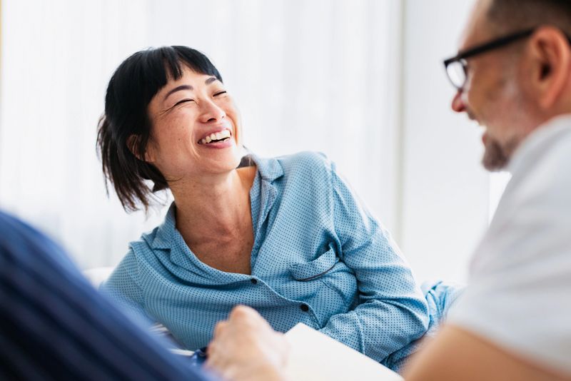 Joyful woman laughs with a friend in a bright, friendly room, creating a warm, candid moment.