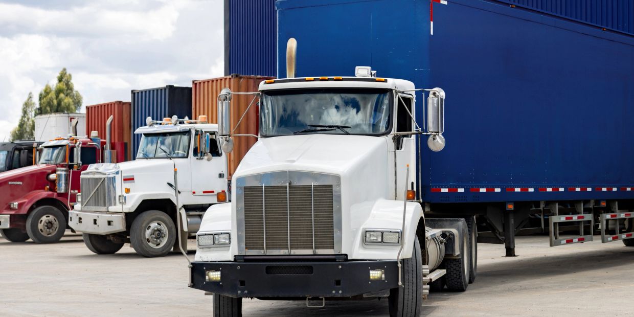 White semi truck with blue trailer and other trucks in background.